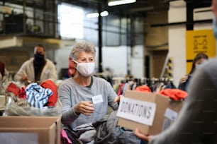 Portrait of volunteers sorting out donated clothes in community charity donation center, coronavirus concept.