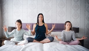 Portrait of mother with daughters doing yoga meditation exercise indoors at home.