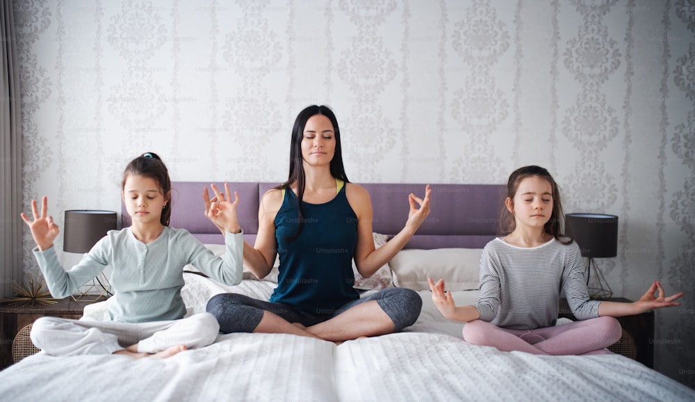 Retrato de una madre con sus hijas haciendo ejercicio de meditación de yoga en el interior de la casa.