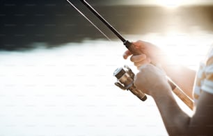 Un tronco di un uomo che pesca in riva a un lago, tenendo in mano una canna. Un primo piano.