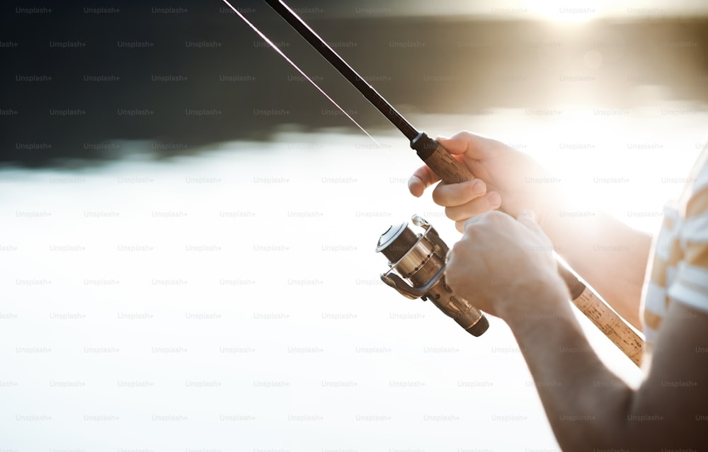 A midsection of a man fishing by a lake, holding a rod. A close-up.