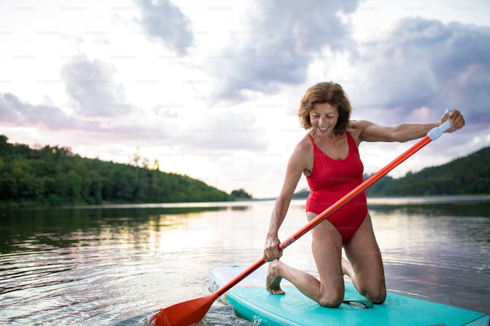 Front view of senior woman paddleboarding on lake in summer. Copy space.
