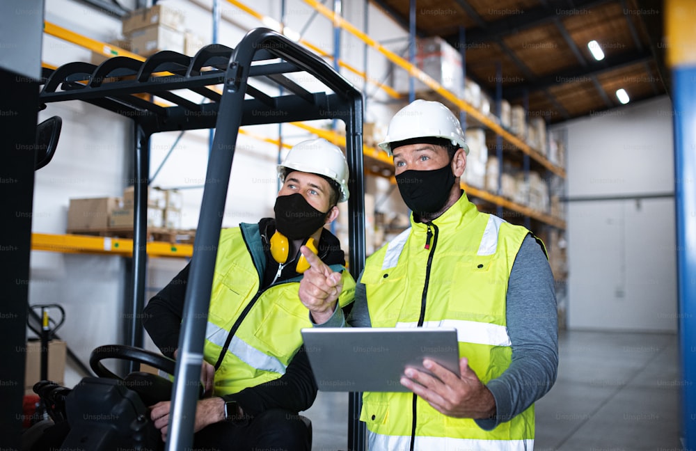 Arbeiter mit Tablet und Gesichtsmaske arbeiten drinnen im Lager, Coronavirus-Konzept.