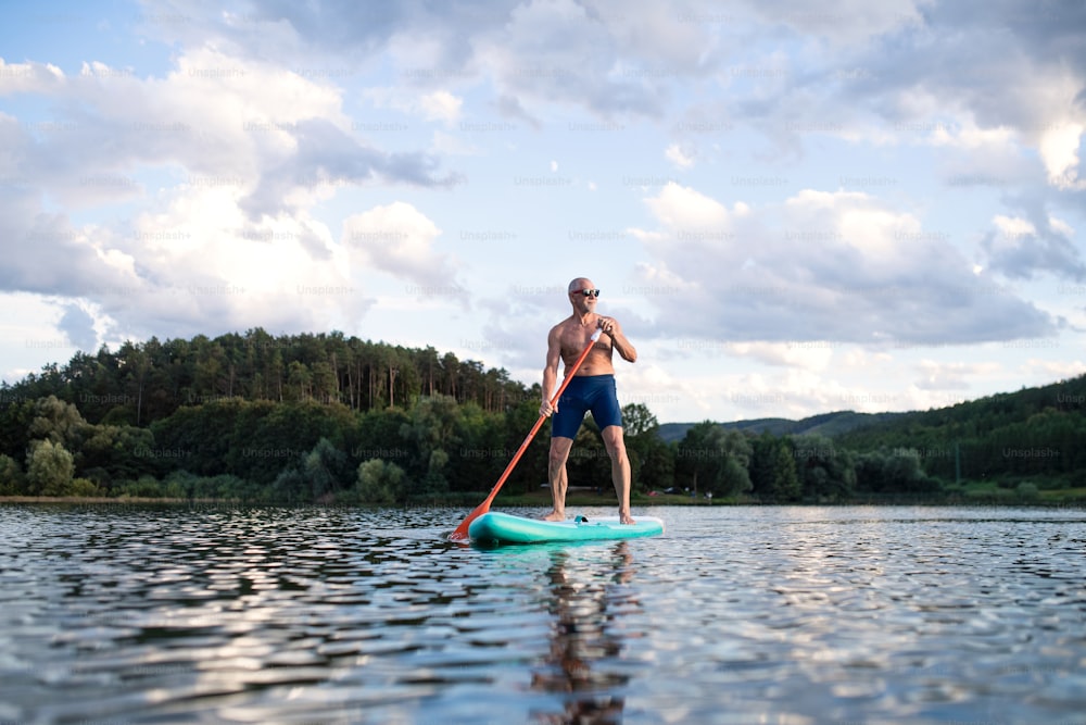 Front view of senior man paddleboarding on lake in summer. Copy space.