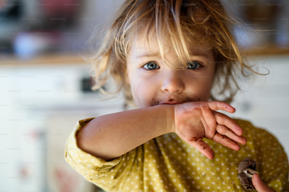 Fröhliches kleines Mädchen mit schmutzigem Mund drinnen in der Küche zu Hause, in die Kamera schauend.