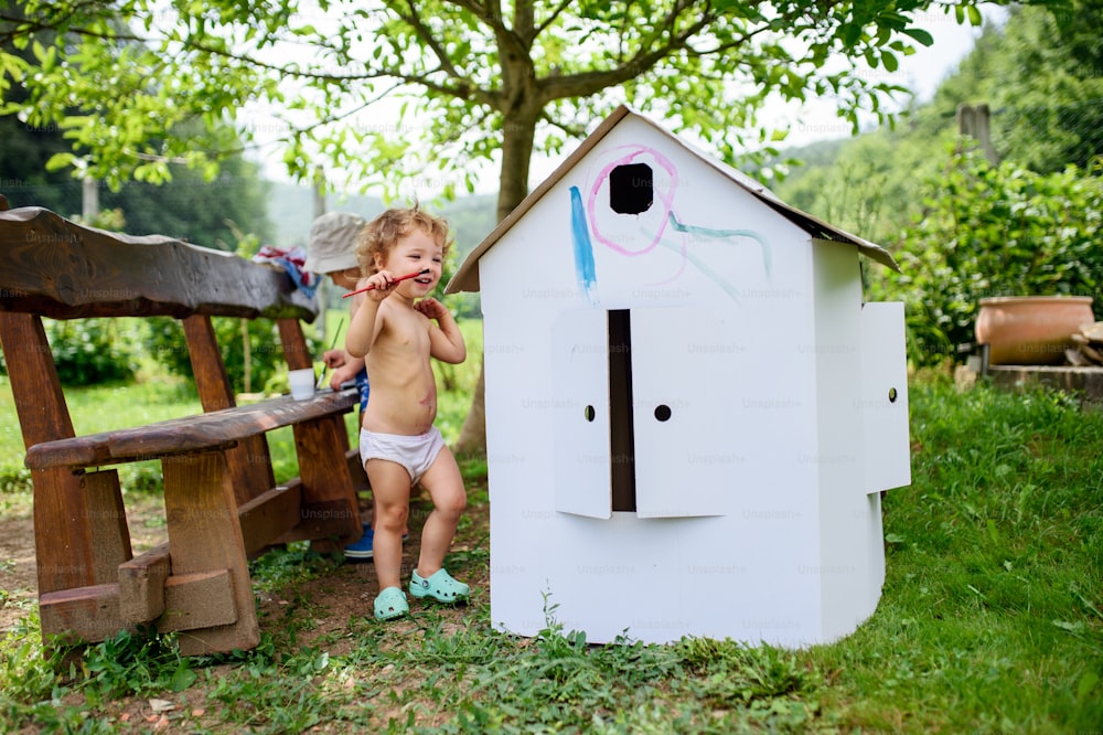 Retrato de niño y niña rubios pequeños en topless pintando al aire libre en verano.