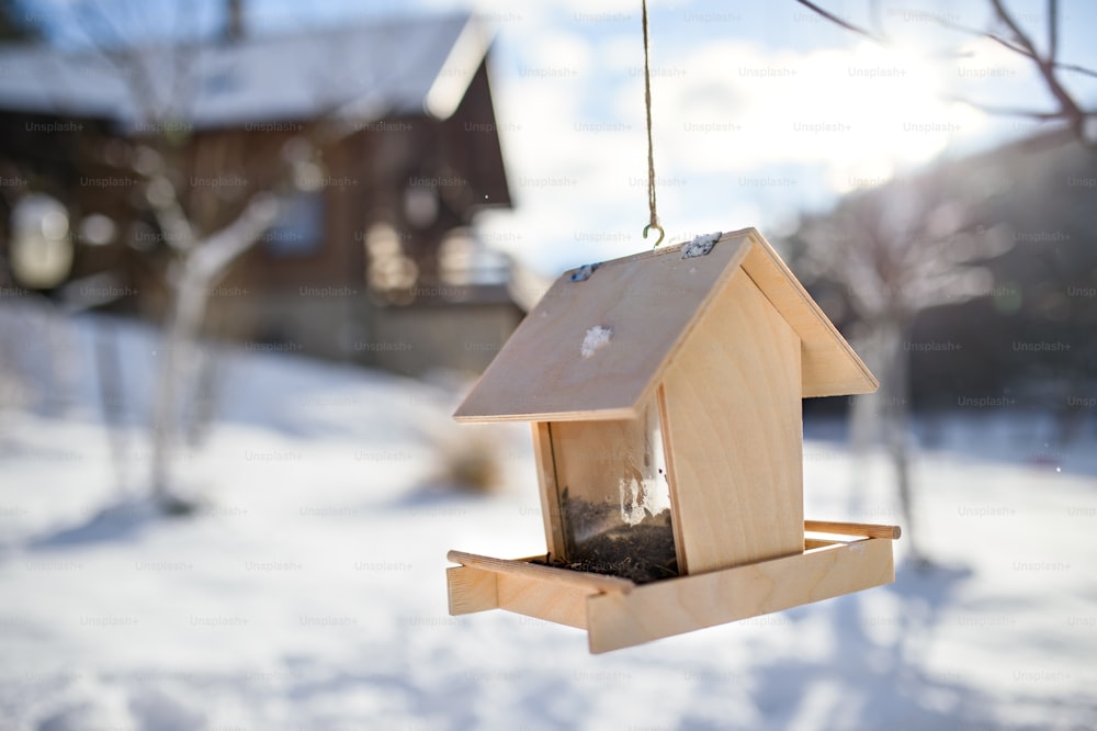 A wooden bird feeder with seeds handging from tree in winter garden.
