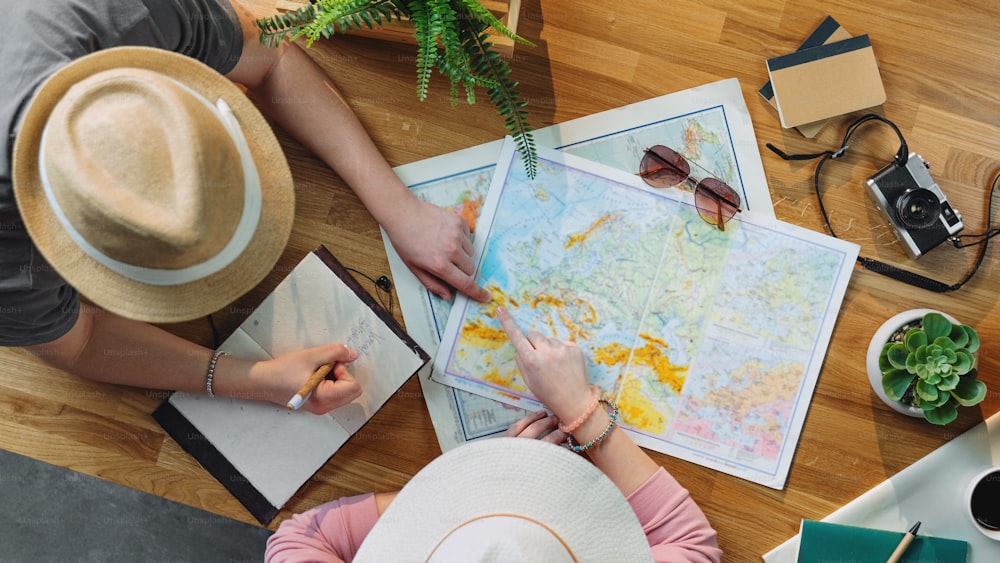 休暇旅行の休日、デスクトップ旅行のコンセプトを計画している地図を持つ認識できない若いカップルの上面図。