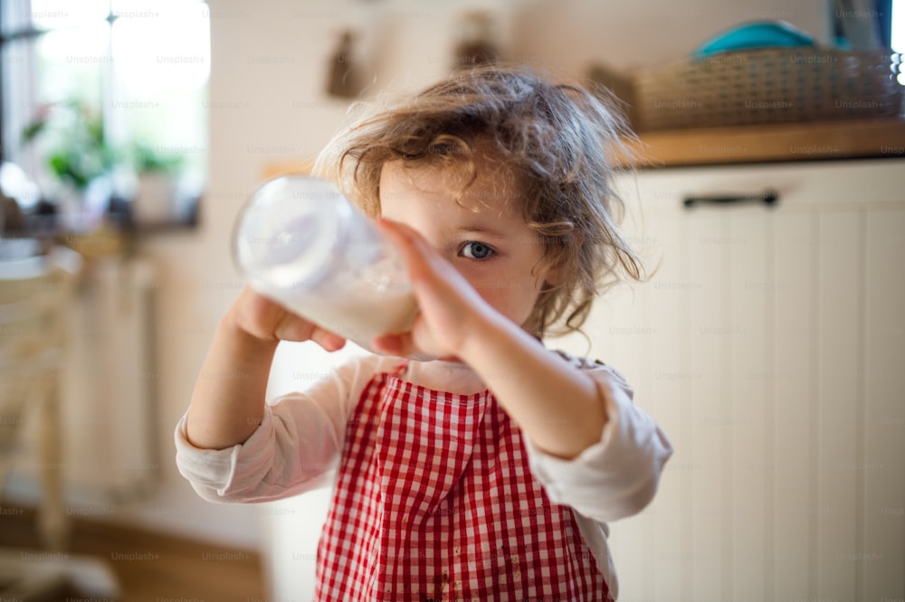 自宅の台所で屋内で小さな女の子の肖像画、哺乳瓶からミルクを飲んでいます。