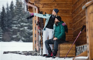 Happy mature couple resting by wooden hut outdoors in winter nature, cross country skiing.