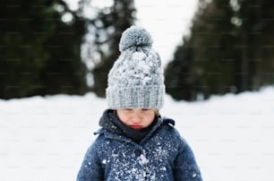 Front view of unhappy and sad small child standing in snow, holiday in winter nature.