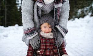 Midsection of unrecognizable mother with small daughter standing in winter nature.