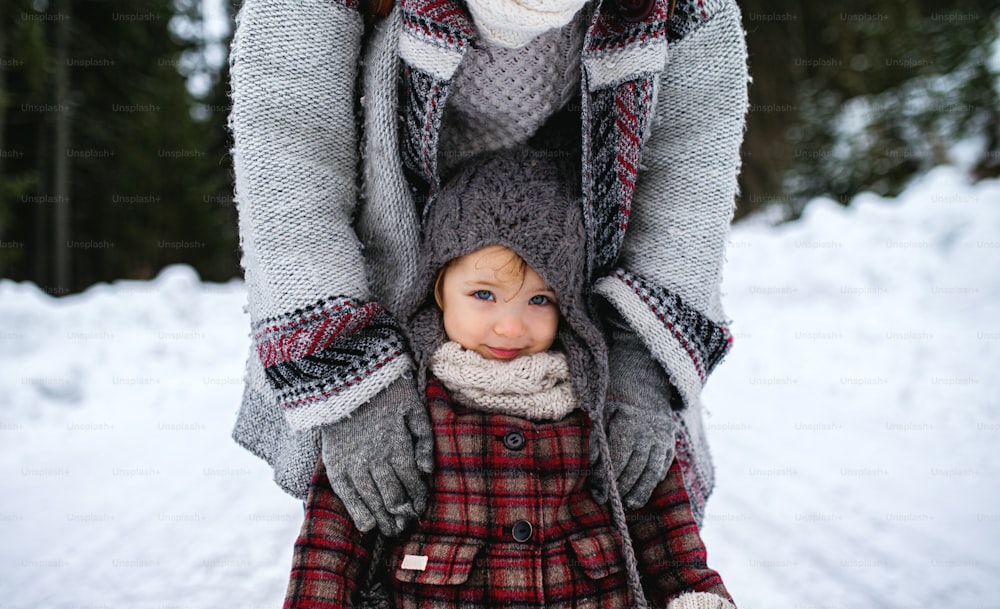 Sezione centrale di madre irriconoscibile con la figlia piccola in piedi nella natura invernale.