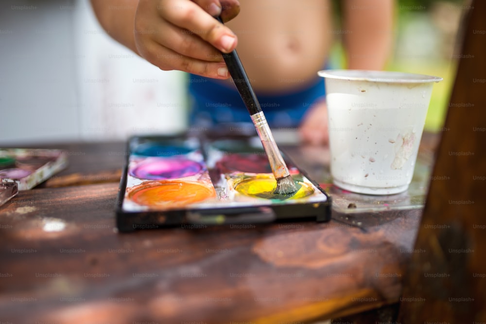 Sección media de un niño irreconocible pintando al aire libre en verano, primer plano.