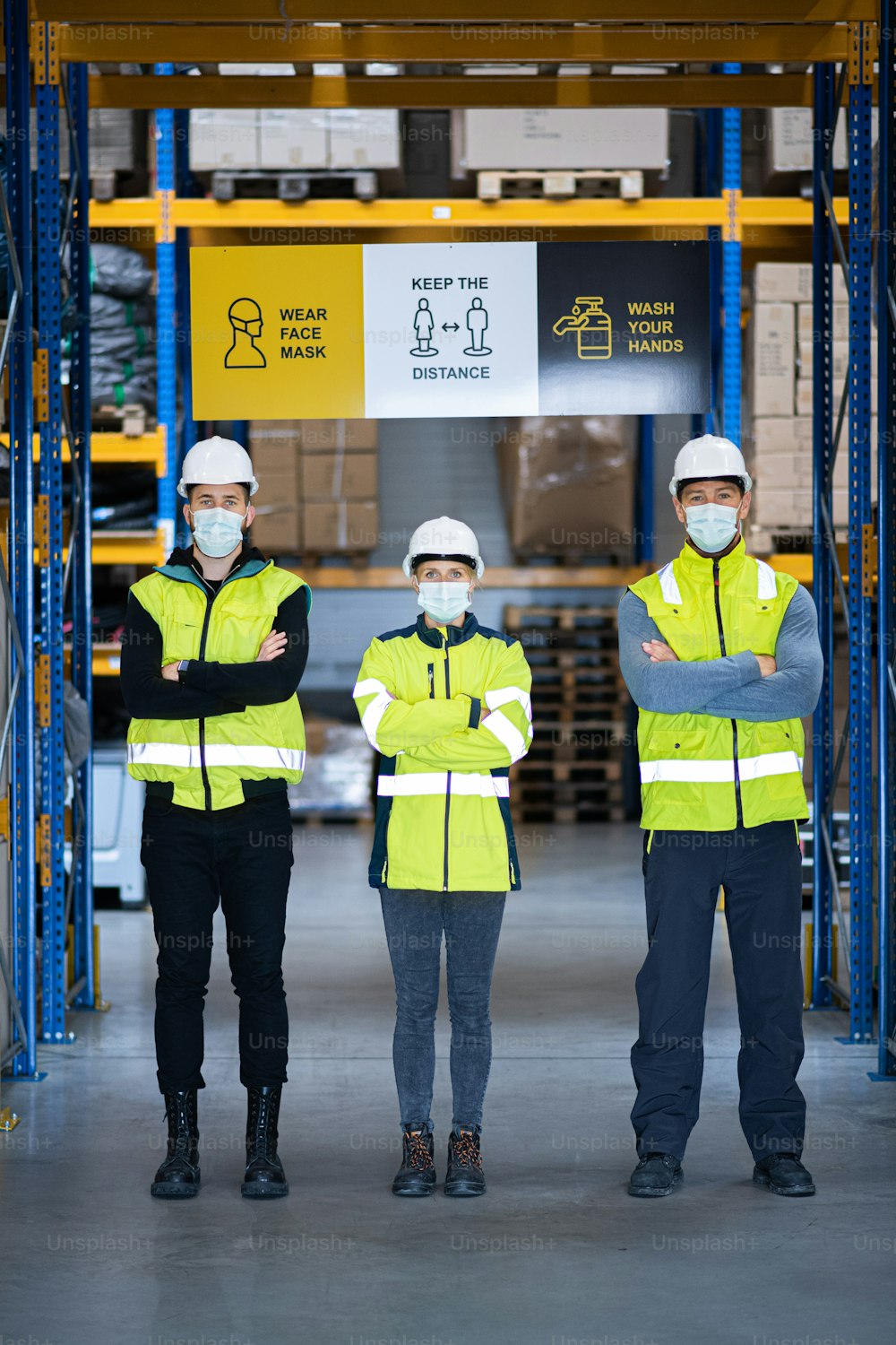 Gruppe von Arbeitern mit Gesichtsmaske steht und schaut in die Kamera im Lager, Coronavirus-Konzept.