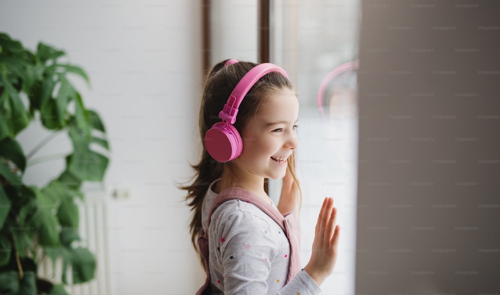 Retrato de una niña feliz con auriculares en el interior de la casa, escuchando música.
