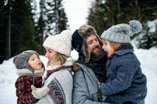Side view portrait of father and mother with two small children in winter nature, standing in the snow.