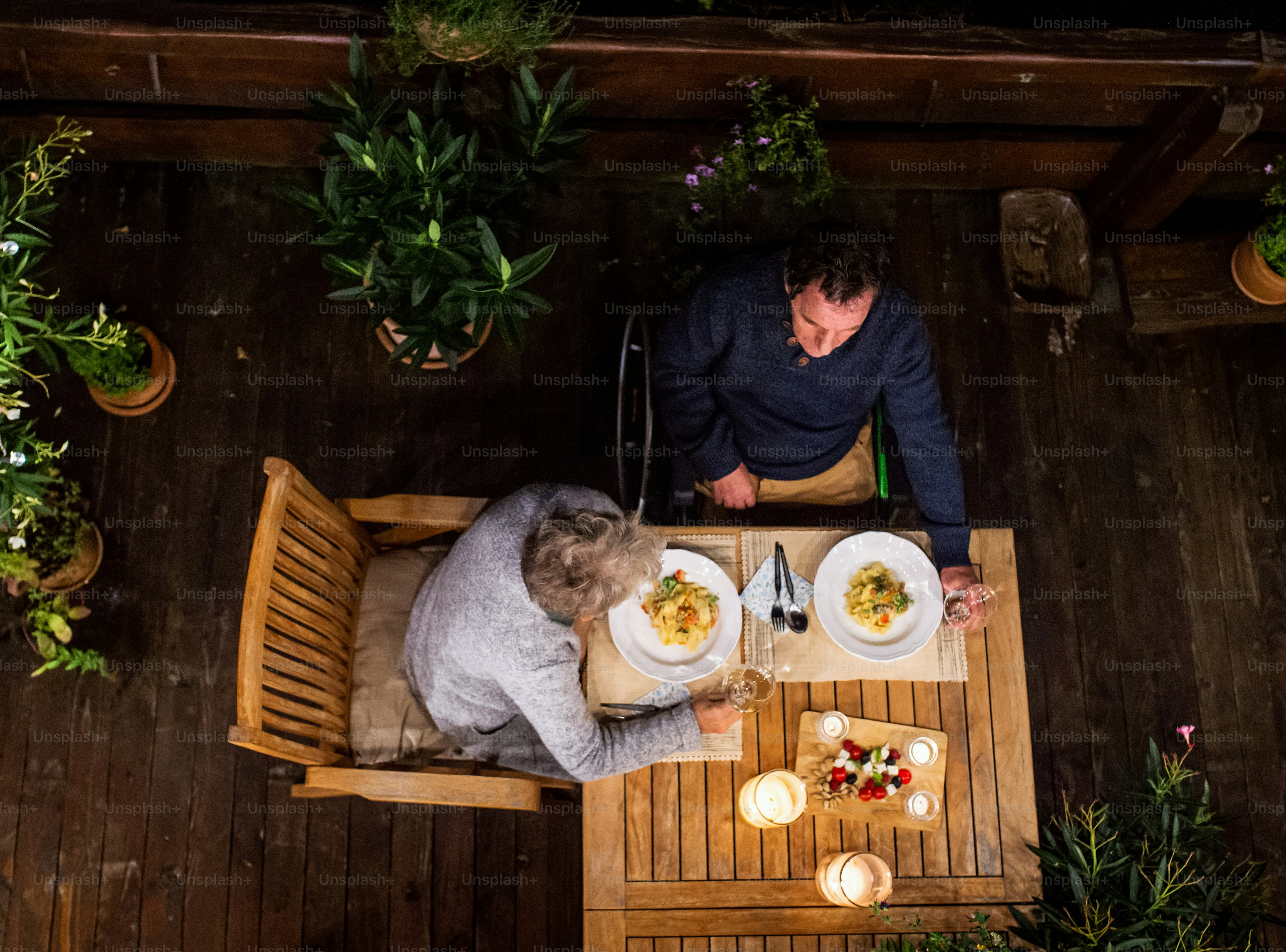 Top view of senior couple in wheelchair having dinner in the evening on terrace, relaxing.