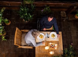 Vista superior de una pareja de ancianos en silla de ruedas cenando por la noche en la terraza, relajándose.