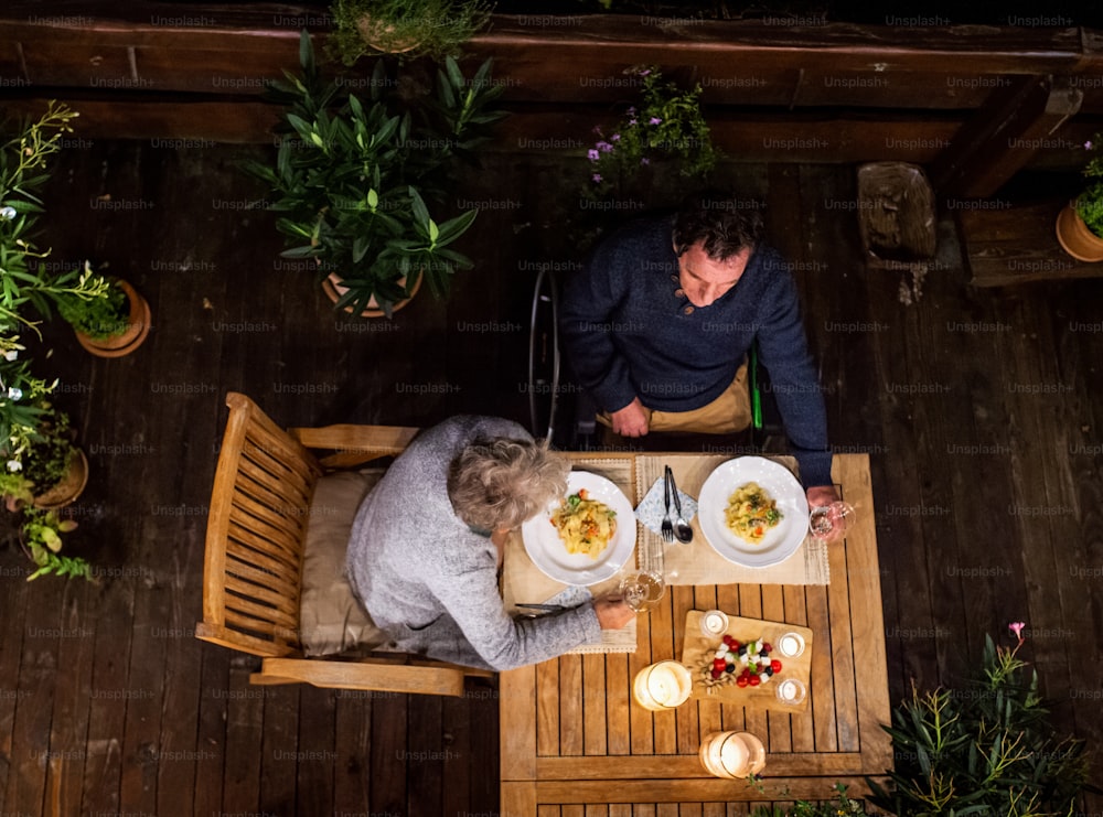 Vista superior do casal idoso em cadeira de rodas jantando à noite no terraço, relaxando.