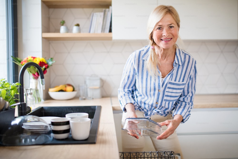 自宅で屋内で皿を�洗う幸せな年配の女性の肖像画。