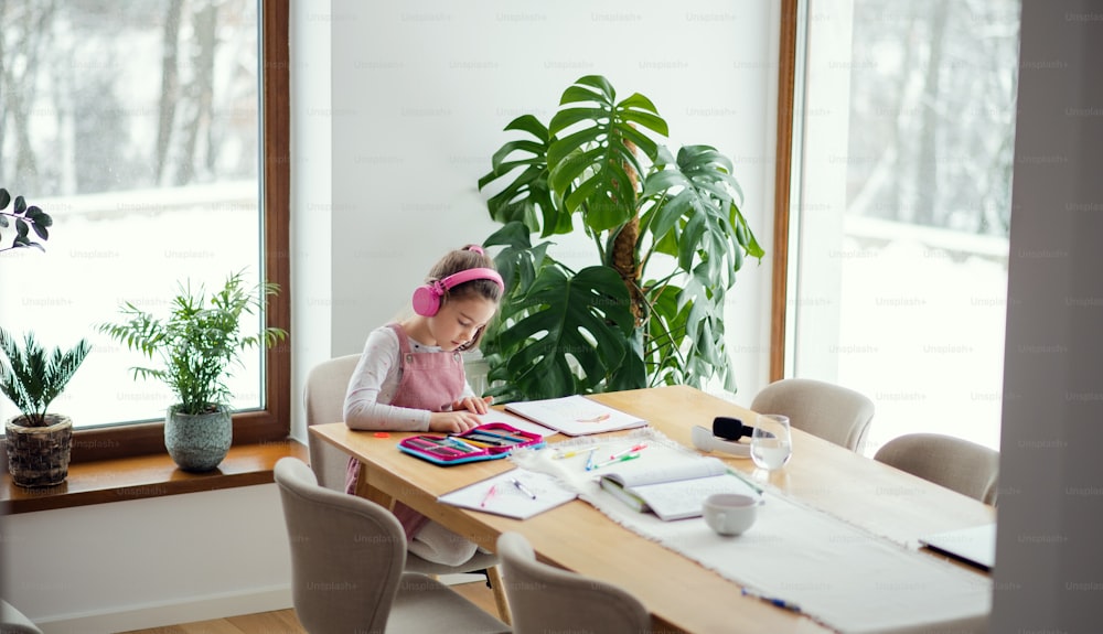 School girl with headphones sitting and working at table indoors at home, distance learning.