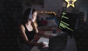 Young girl with headphones and computer sitting indoors, playing games and hacker concept.