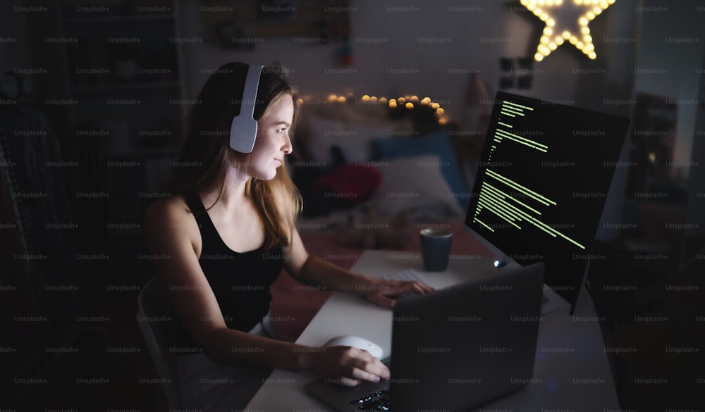 Junges Mädchen mit Kopfhörern und Computer sitzt drinnen, spielt Spiele und Hacker-Konzept.