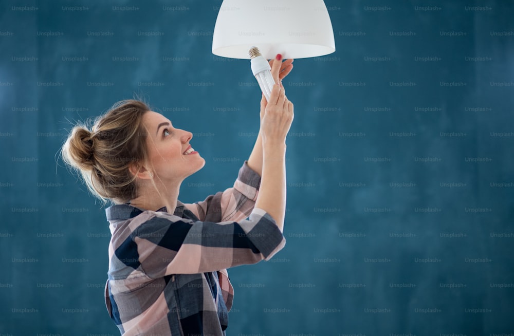 Portrait d’une femme heureuse changeant l’ampoule à l’intérieur à la maison, déménagement et concept de bricolage.