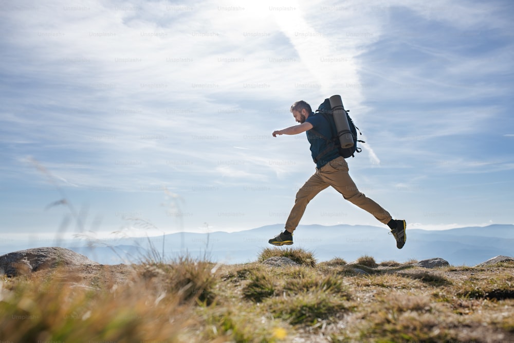 Vista lateral de un hombre maduro con mochila caminando por las montañas en verano, saltando.