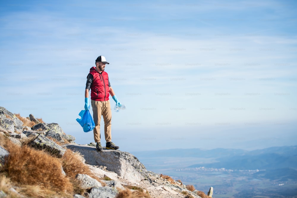 Escursionista uomo maturo che raccoglie rifiuti in natura in montagna, concetto di plogging.