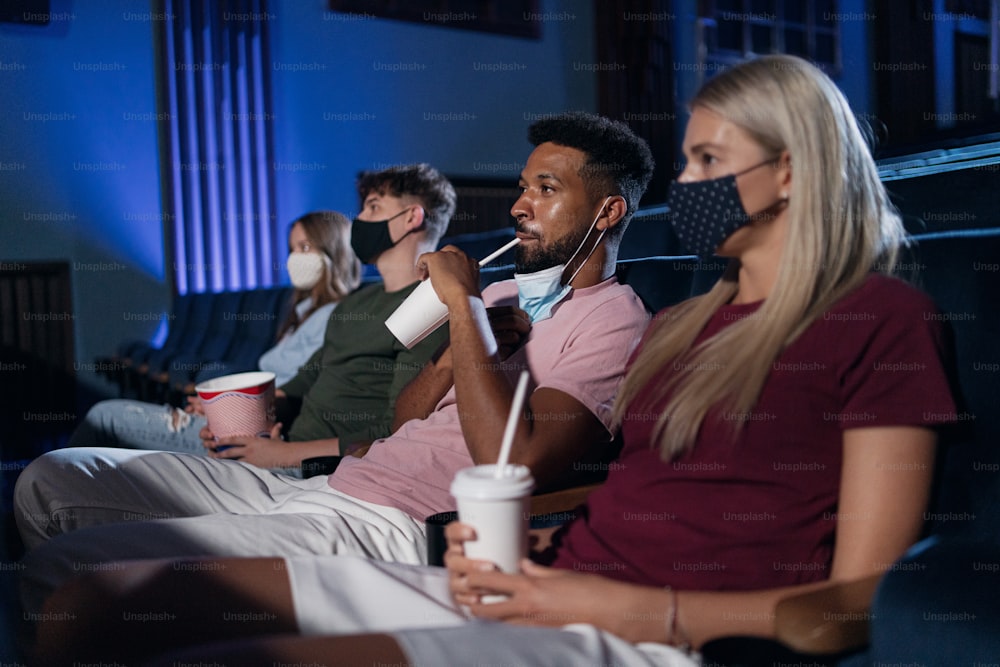 Young people watching a film in the cinema, coronavirus concept.