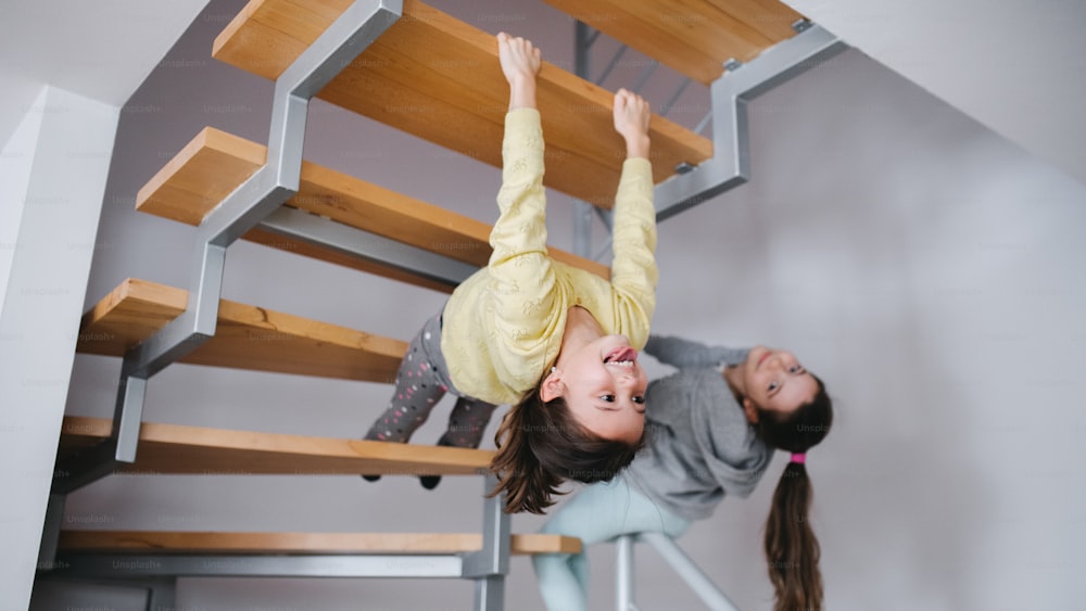 두 명의 쾌활한 작은 소녀 자매가 집 실내에서 계단 아래에서 즐거운 시간을 보내고 있습니다.