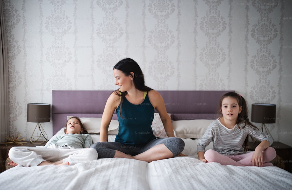 Portrait of mother with daughters on bed after exercise indoors at home.