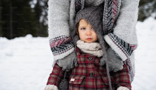 Seção média de mãe irreconhecível com filha pequena em pé na natureza do inverno.