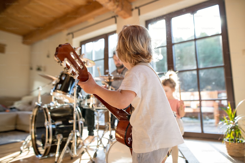 Rear view of small boy with a family indoors at home, playing guitar.