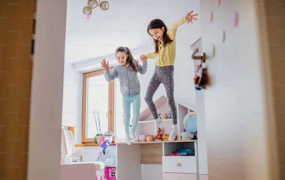 Two cheerful small girls sisters indoors at home, jumping on bed in bedroom.