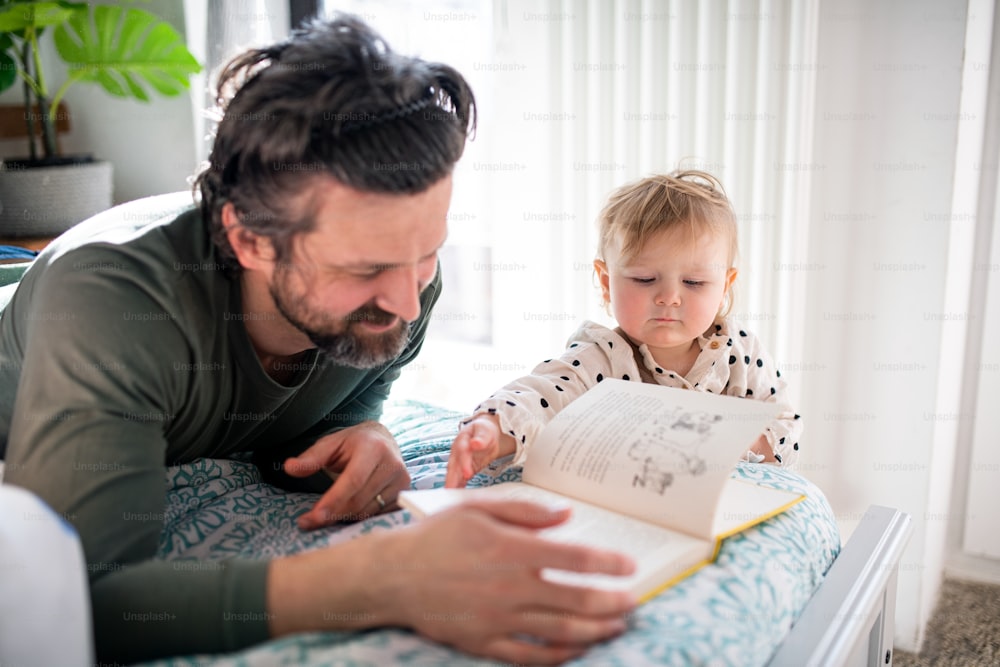 Père avec une petite fille heureuse lisant un livre à l’intérieur à la maison.