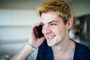 Close-up of happy young man with smartphone indoors at home, making phone call.