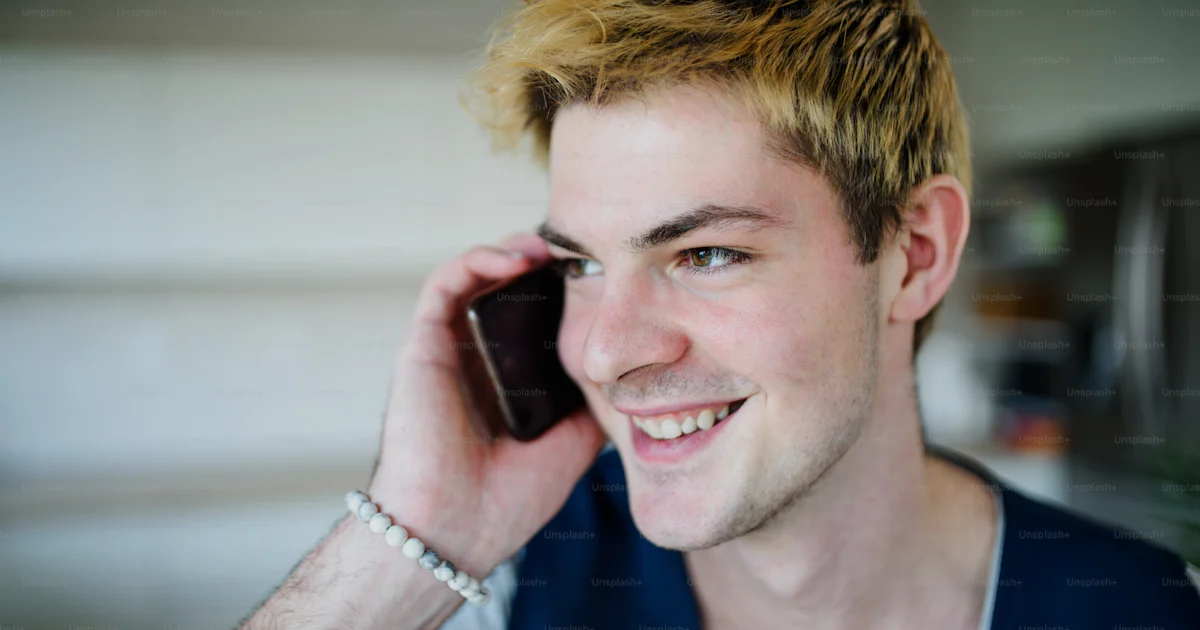 Close-up of happy young man with smartphone indoors at home, making ...