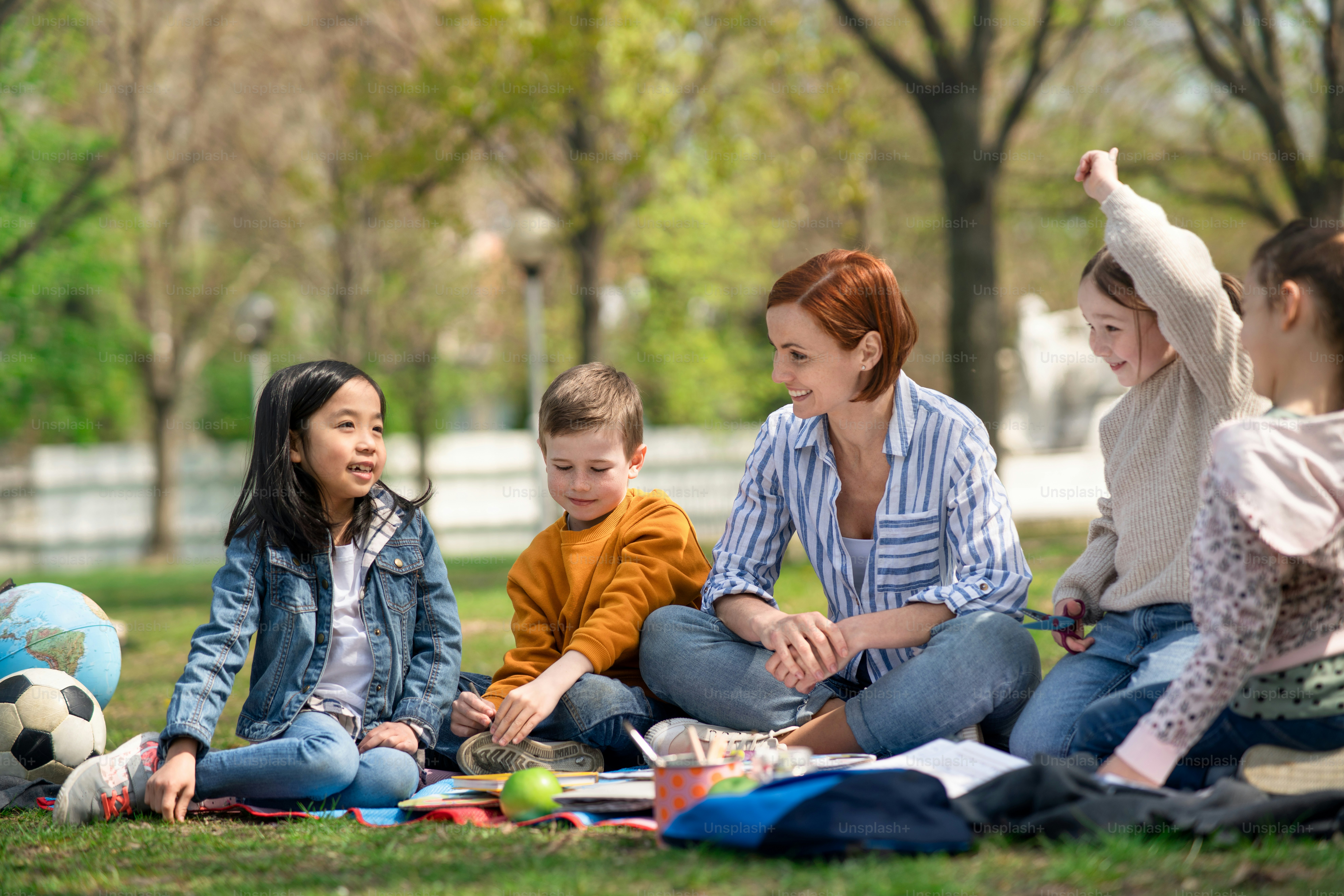 Um professor com crianças pequenas sentadas ao ar livre no parque da cidade, aprendendo conceito de educação em grupo