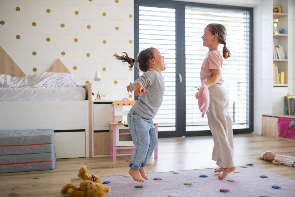 女の子の姉妹が家で室内で遊んでいて、ジャンプしているポートレート。