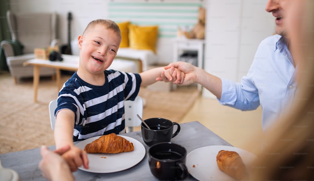 A portrait of happy down syndrome boy with parents at the table, having breakfast.