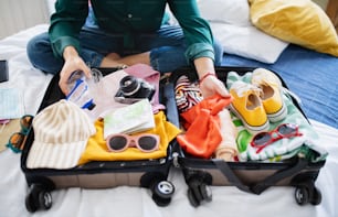 Unrecognizable young woman with suitcase packing for holiday at home, coronavirus concept.