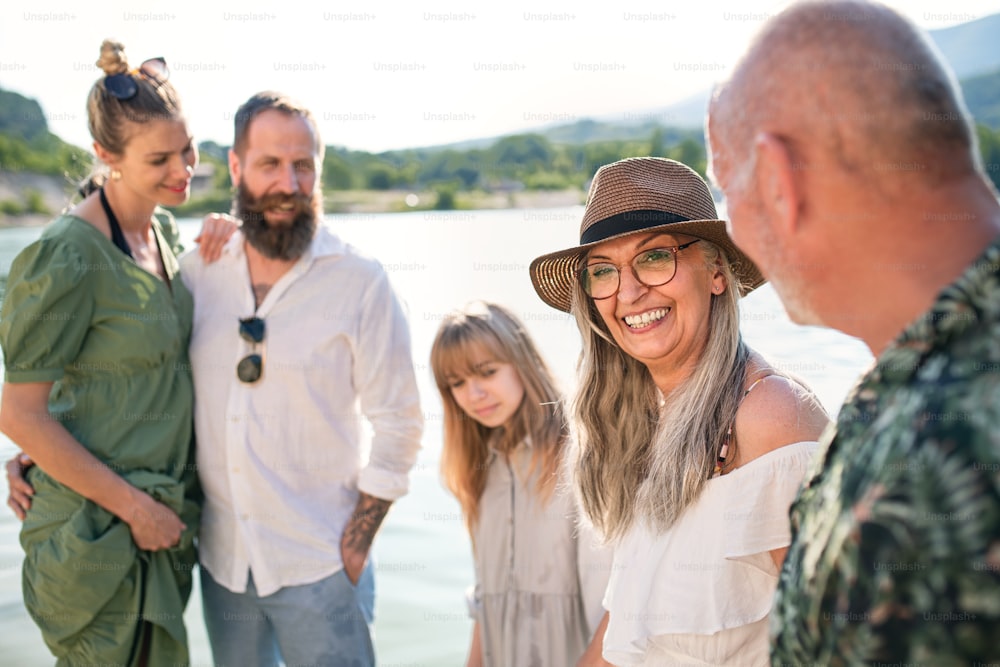 Portrait d’une famille multigénérationnelle heureuse en vacances d’été, se promenant au bord d’un lac.