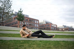 Un hombre con auriculares y teléfono inteligente al aire libre en un parque de la ciudad, descansando.