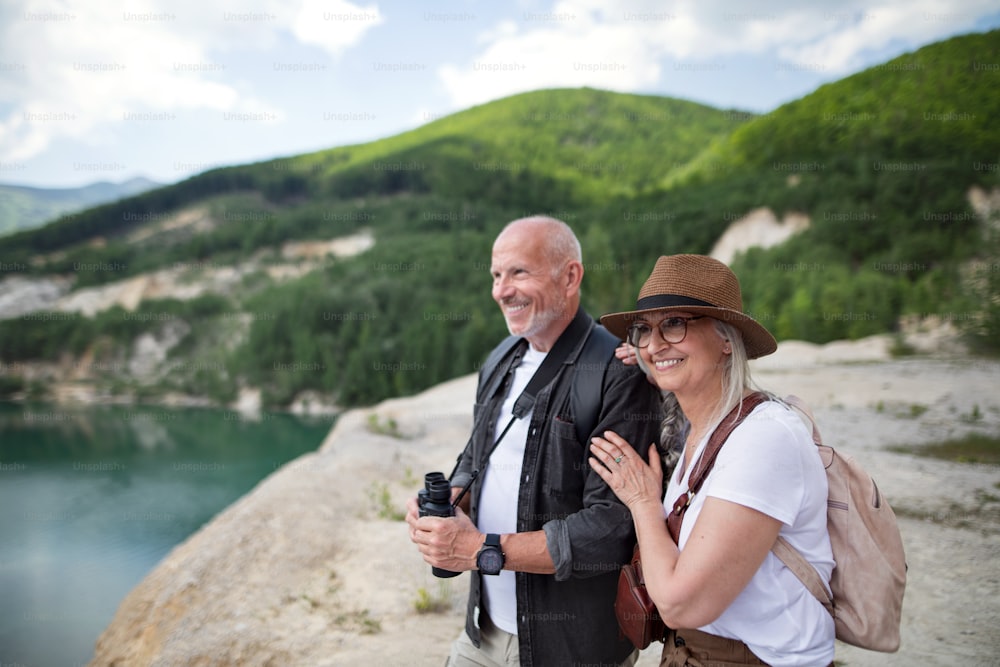 A happy senior couple on hiking trip on summer holiday, looking at scenery.