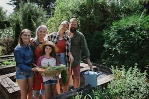 Eine glückliche Bauernfamilie, die in die Kamera schaut und ihre Ernte im Garten hält.