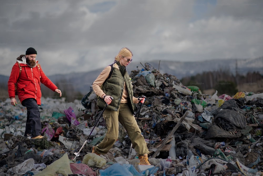 Man and woman hikers with walking poles on landfill, environmental and pollution concept.