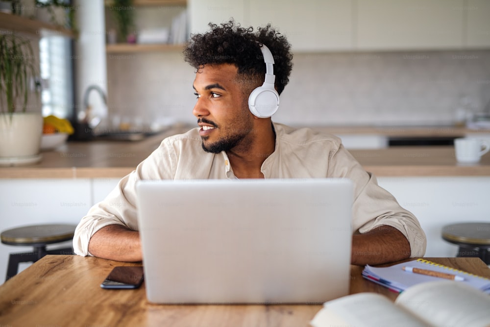 Portrait of young man student with laptop and headphones indoors at home, studying.